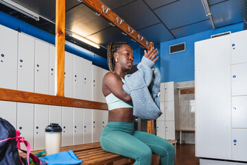 Young female athlete taking off her sweater in gym locker room after workout