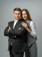 Portrait of confident young man in formal suit standing with arms crossed next to stylish young woman in pantsuit. Studio shoot . Business fashion, professional team concept