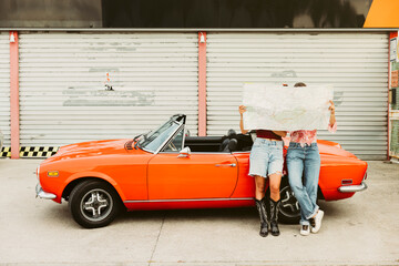 Tourists holding map planning road trip with vintage orange convertible car