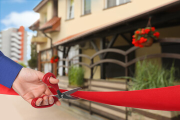 Man cutting red ribbon at opening ceremony of restaurant, closeup
