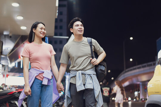 Couple enjoying a night stroll through vibrant streets of Hanoi, Vietnam, hand in hand under city lights