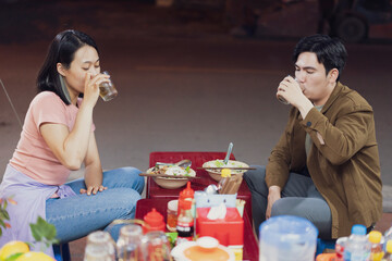 Friends enjoy a casual meal and drinks together at a street food stall in Hanoi, Vietnam during an evening outing