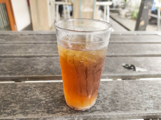 A glass of tea filled with ice cubes on a wooden table. A refreshing drink to quench your thirst and accompany spicy food in a restaurant. Drink or beverages photography with negative space