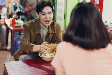 Young man enjoying a meal and drinks with a woman in a Hanoi eatery at night