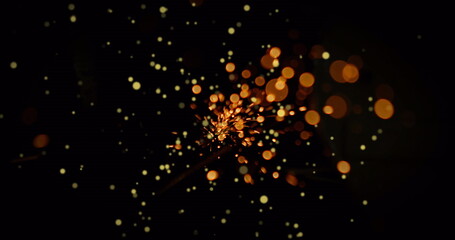 Flickering sparks glowing brightly in dark field, with ember-like light particles