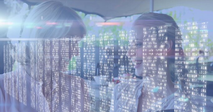 Chatting mother and daughter sipping coffee at sunlit cafe terrace, binary code overlay