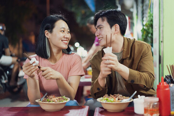 Joyful couple enjoying local Vietnamese cuisine at a street stall in Hanoi during a vibrant evening