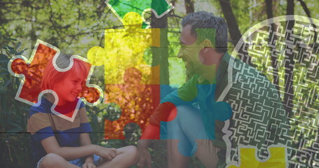 Smiling father and son sharing moment on sunlit clearing, with colorful puzzle maze graphics
