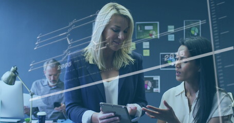 Reviewing tablet, women in business attire collaborating in office with charts and digital overlay