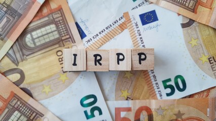 IRPP acronym made of wooden letter cubes on pile of Euro banknotes. Impôt sur le Revenu des...
