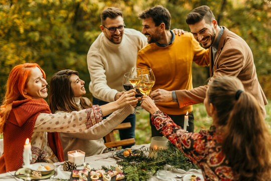 Friends toasting wine glasses celebrating thanksgiving dinner outdoors in forest