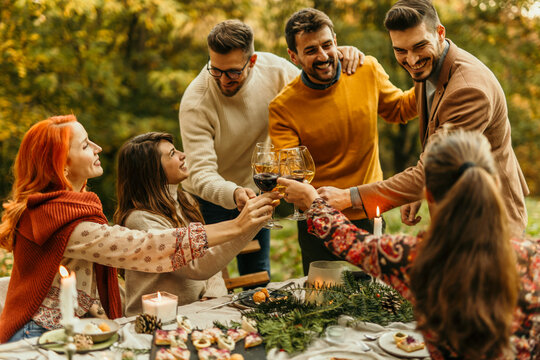 Friends toasting wine glasses, celebrating thanksgiving dinner outdoors in beautiful autumn forest