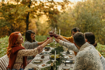 Friends toasting red wine at a festive outdoor autumnal dinner party