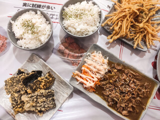 Tabletop shot of Japanese food dishes on white table with japanese text. Japanese food feast consisting of seaweed rice, Beef Yakiniku, crispy Nori and Enoki Tempura. Gourmet and cuisine photography