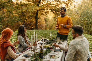 Friends enjoying thanksgiving dinner outdoors in beautiful autumn forest