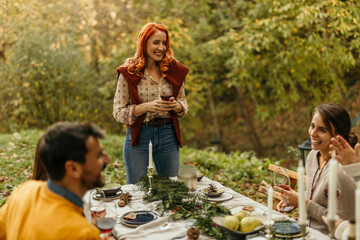 Woman giving toast to friends at outdoor autumnal dinner party
