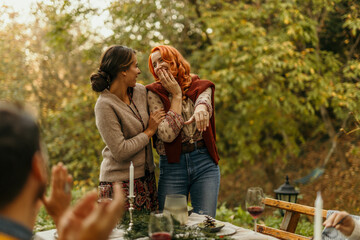 Woman showing engagement ring to her friend celebrating with family outdoors