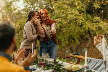 Woman showing engagement ring to friends celebrating at outdoor dinner party