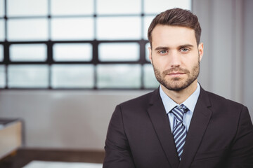 Fototapeta premium Male business professional standing in office by grid window, with blurred desk and wall panel