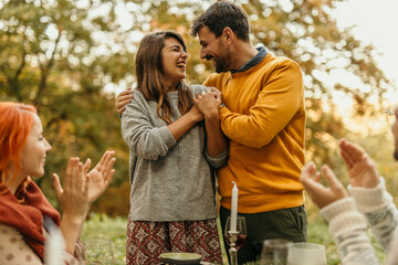 Happy couple embracing while friends are clapping at outdoor autumn party