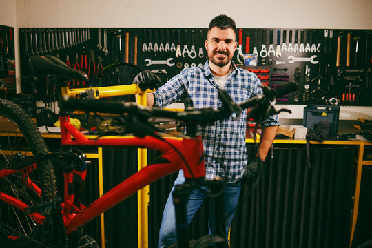 Bicycle mechanic smiling and posing with mountain bike in repair workshop - Powered by Adobe