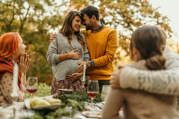 Happy pregnant couple embracing at a festive outdoor gathering with friends