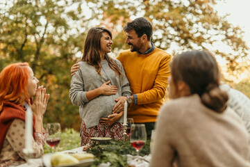 Happy couple expecting baby sharing news with friends at outdoor party