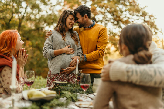 Happy pregnant couple embracing at a festive outdoor gathering with friends