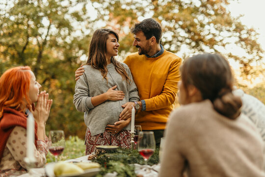 Happy couple expecting baby sharing news with friends at outdoor party