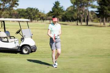 Female golfer standing on putting green holding putter and golf ball near white golf cart