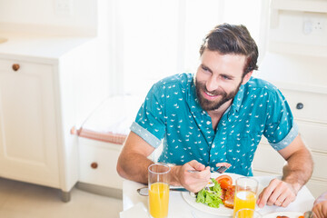 Fork hovering over fresh salad and tomato slices on white dining table in bright kitchen space