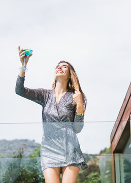 Naklejki Turquoise cocktail gleaming in martini glass on balcony railing under clear sky, wood framing