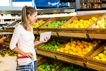 Woman selecting citrus and green apples from bins in produce aisle with metal cart, copy space