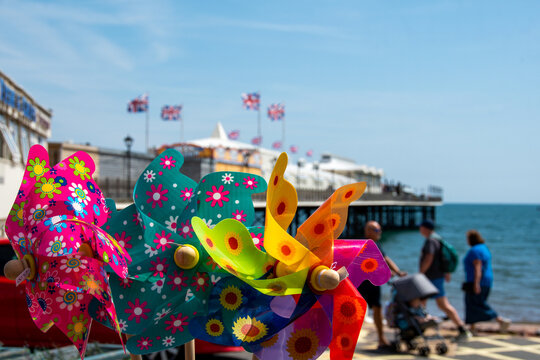 Seaside holiday image with colourful plastic windmills set against a softly focused pier with Union Jack flags flying. British holiday and family holiday. School holidays. Vertical image.