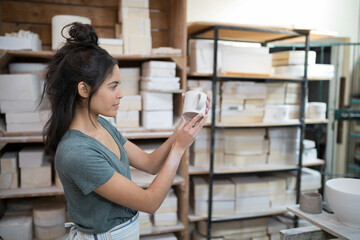 White ceramic mug sitting on worktable among shelves of plaster molds and bisque forms, copy space