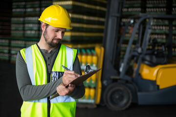 Man wearing safety vest, hardhat writing on clipboard with pen by forklift in warehouse, copy space © WavebreakMediaMicro