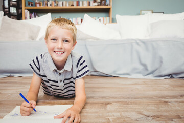 Naklejka premium School-age boy wearing striped polo drawing with blue marker on paper in living room