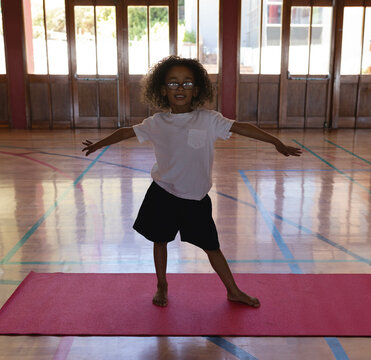 Fototapeta Child balancing on red yoga mat on wooden gym floor, with sunlight streaming through glass doors