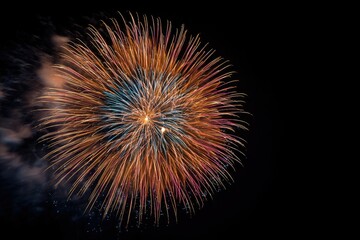 A vibrant firework display explodes in a circular burst of orange, pink, and blue against a stark black night sky, creating a dazzling spectacle of light and color