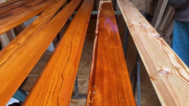 A brush applies wood stain to raw planks, revealing a rich amber finish. This satisfying transformation highlights craftsmanship, woodwork process, and surface treatment in a workshop setting.