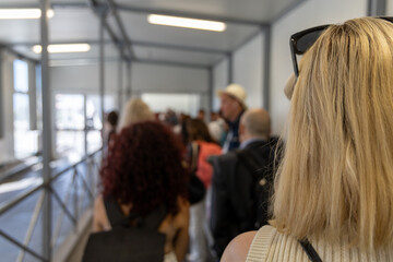 People standing in line at an airport boarding gate, with a blonde woman in casual clothes clearly...