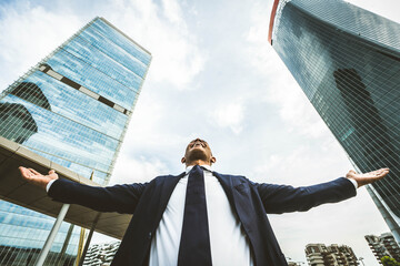 Happy business man with arms up standing in front of office buildings - Successful businessman celebrating victory outside