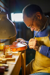 Skilled luthier carefully applying varnish to violin, surrounded by specialized woodworking tools in traditional workshop, showcasing meticulous instrument crafting process