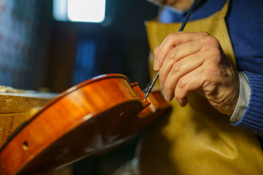 Skilled craftsman brushing fine varnish onto violin body, highlighting woodworking precision and traditional lutherie techniques in well lit workshop setting