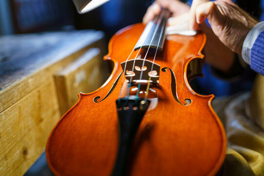 Skilled luthier carefully polishing wooden violin body, highlighting precision woodworking and traditional instrument crafting techniques in workshop setting