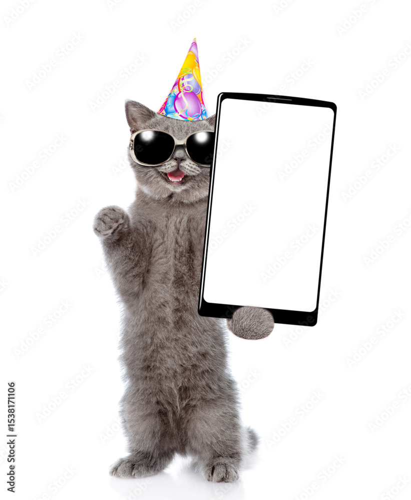 Poster Laughing cat with open mouth wearing sunglasses and party cap standing on hind legs and showing big smartphone with blank screen. Empty space for text. isolated on white background