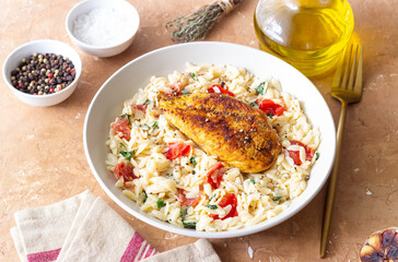 Orzo pasta with fried chicken breast, tomatoes and herbs. Italian food.