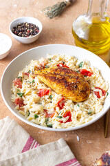 Orzo pasta with fried chicken breast, tomatoes and herbs. Italian food.