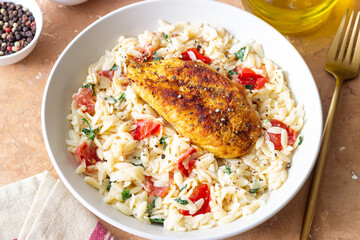Orzo pasta with fried chicken breast, tomatoes and herbs. Italian food.