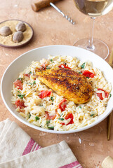 Orzo pasta with fried chicken breast, tomatoes and herbs. Italian food.